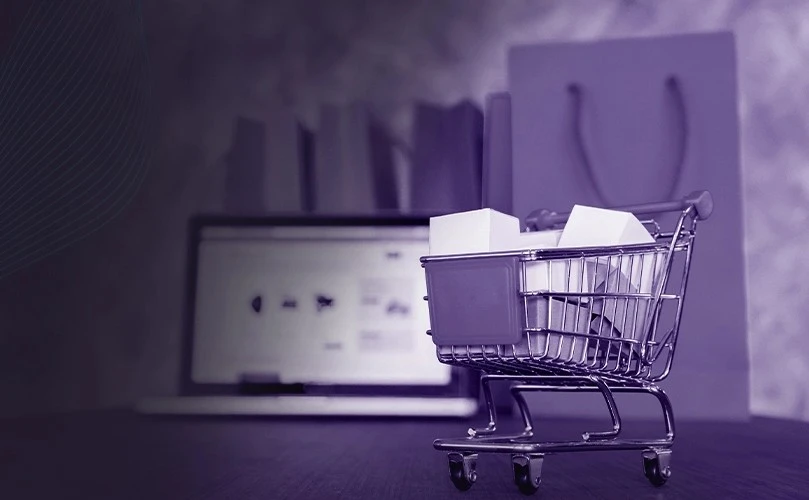 Shopping cart with packages in front of a laptop and retail bags, representing retail IT solutions that streamline multi-branch operations, supplier management, and retail efficiency.